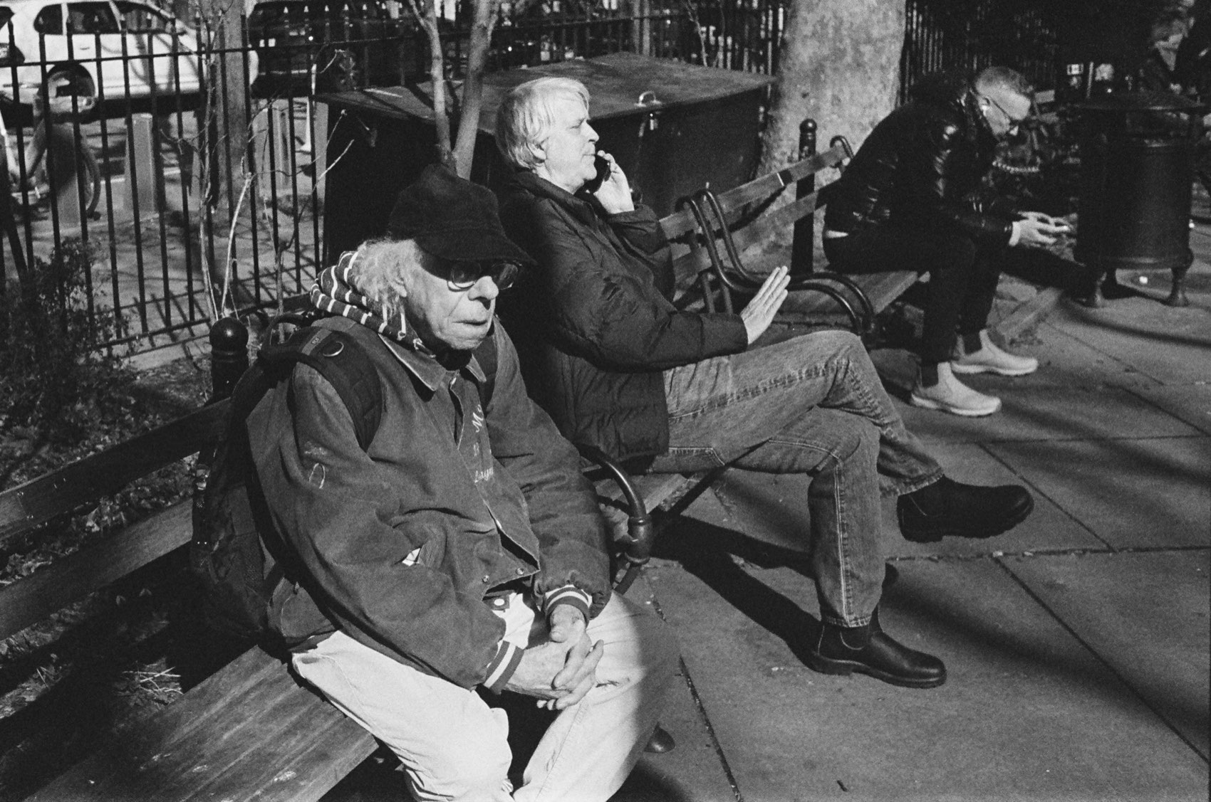 People sitting along a park bench behind iron railings.