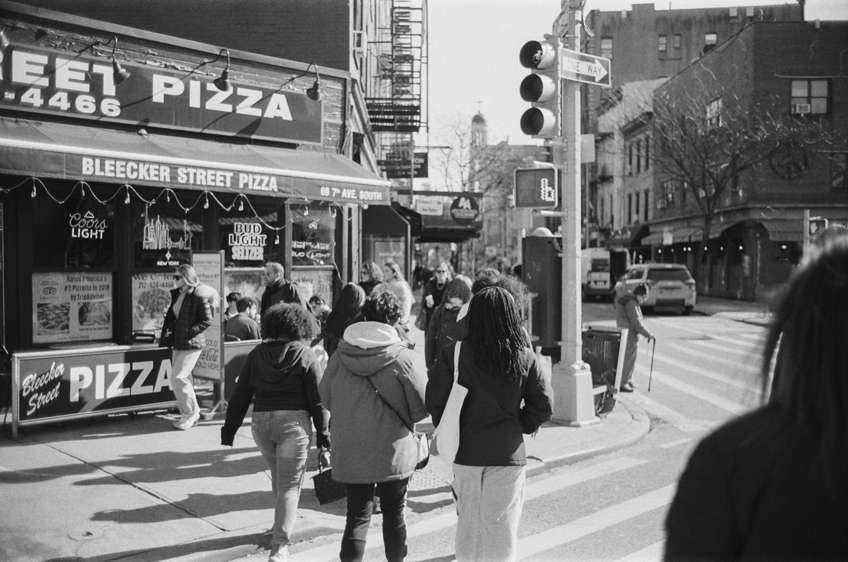 The Bleecker Street Pizza corner in daylight, people crossing.
