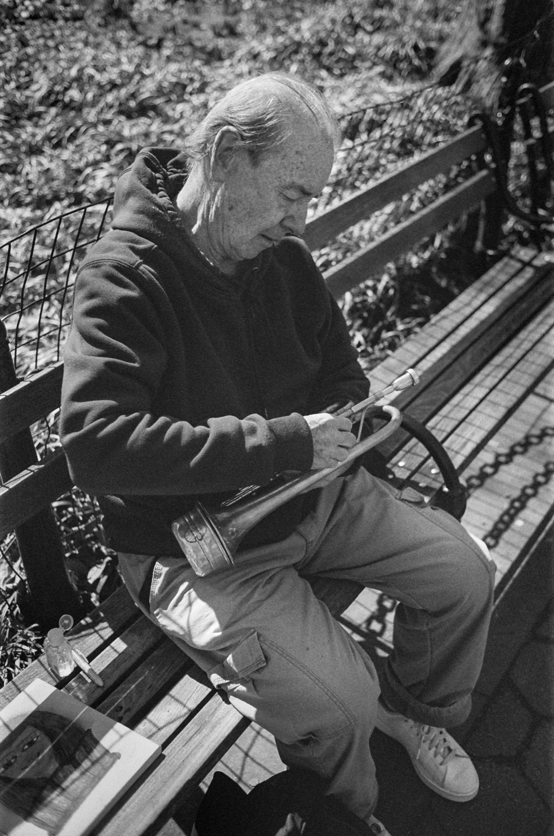 A man on a park bench with a trumpet across his lap.