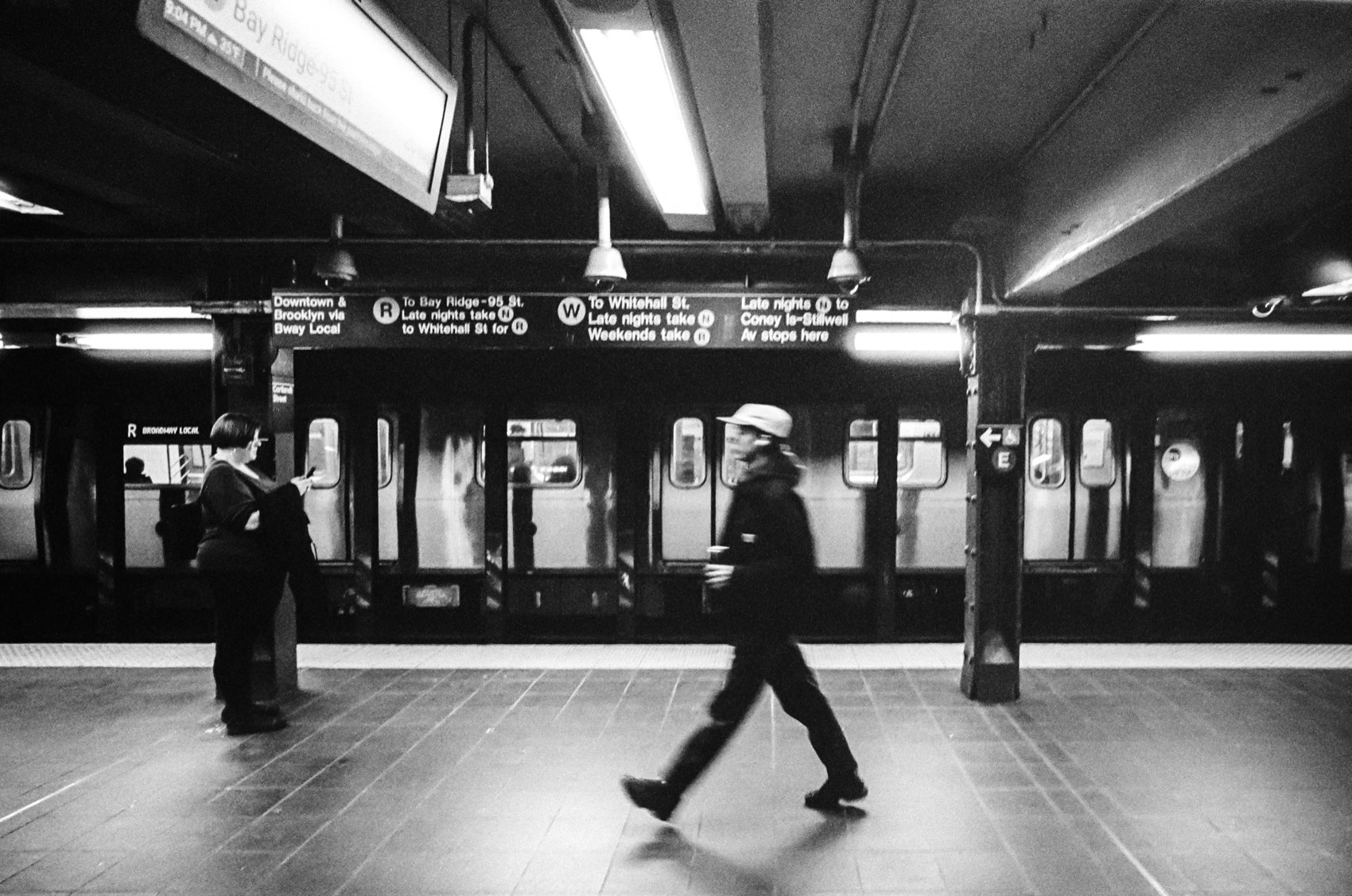 A subway platform at night, one figure walking past a waiting train.