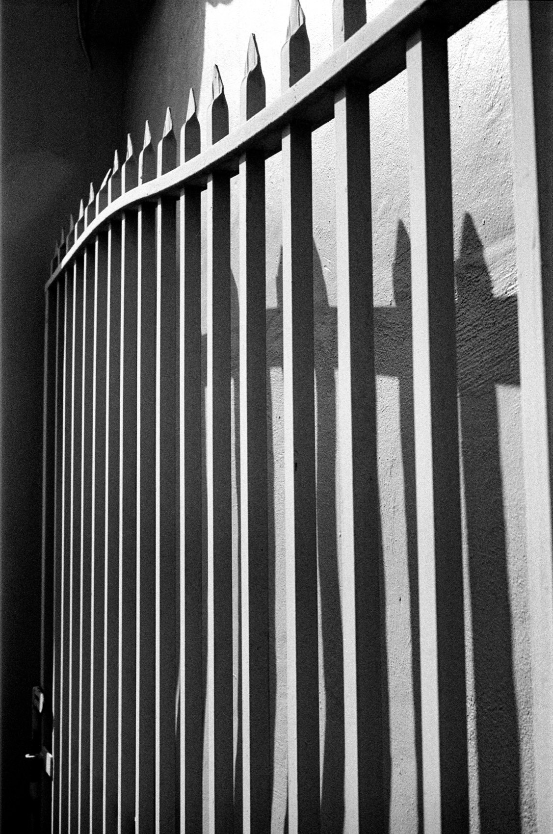 Spiked railings throwing their own shadow flat against a pale wall.