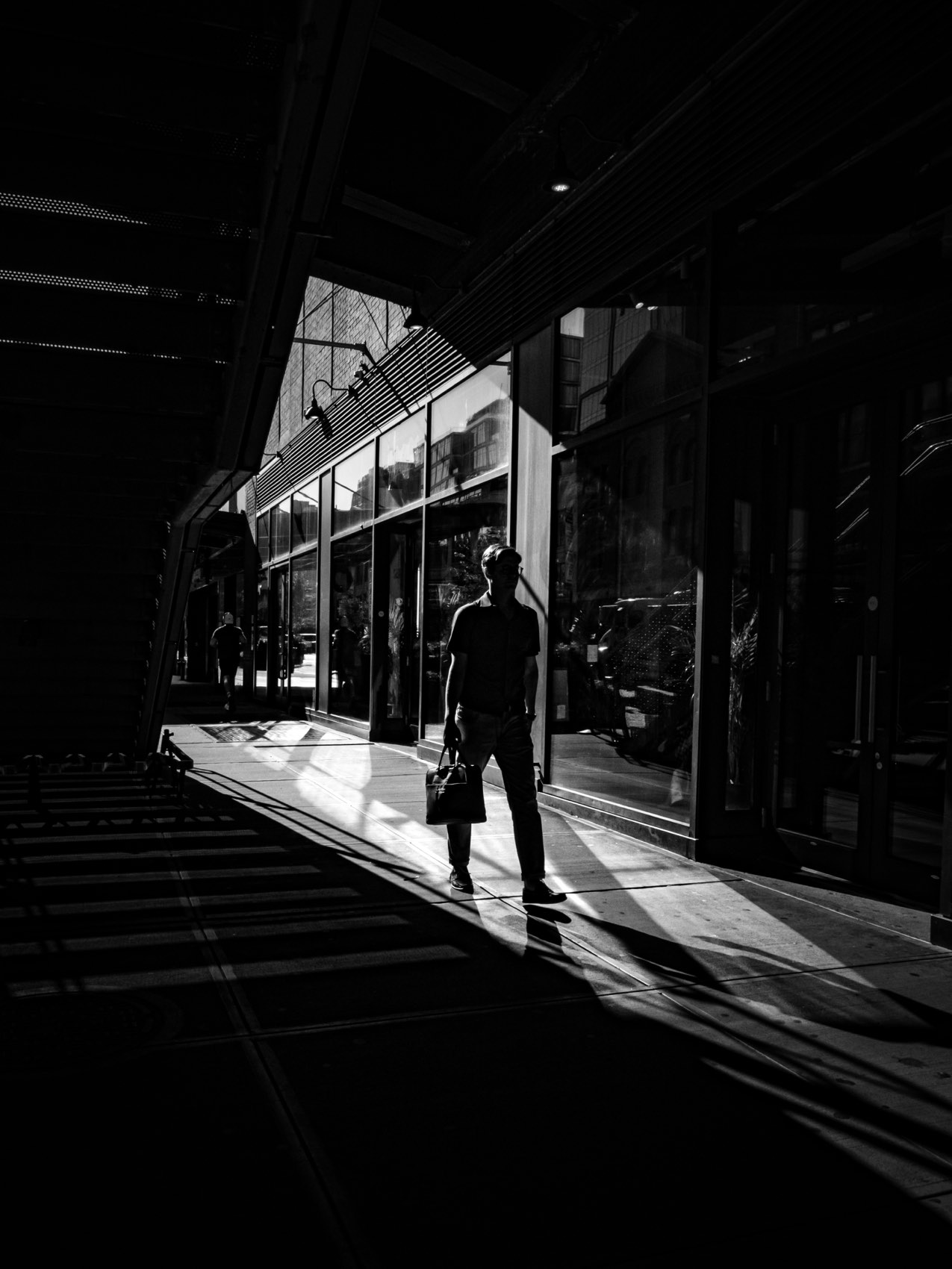 A figure crossing a bright patch of light between two dark buildings.