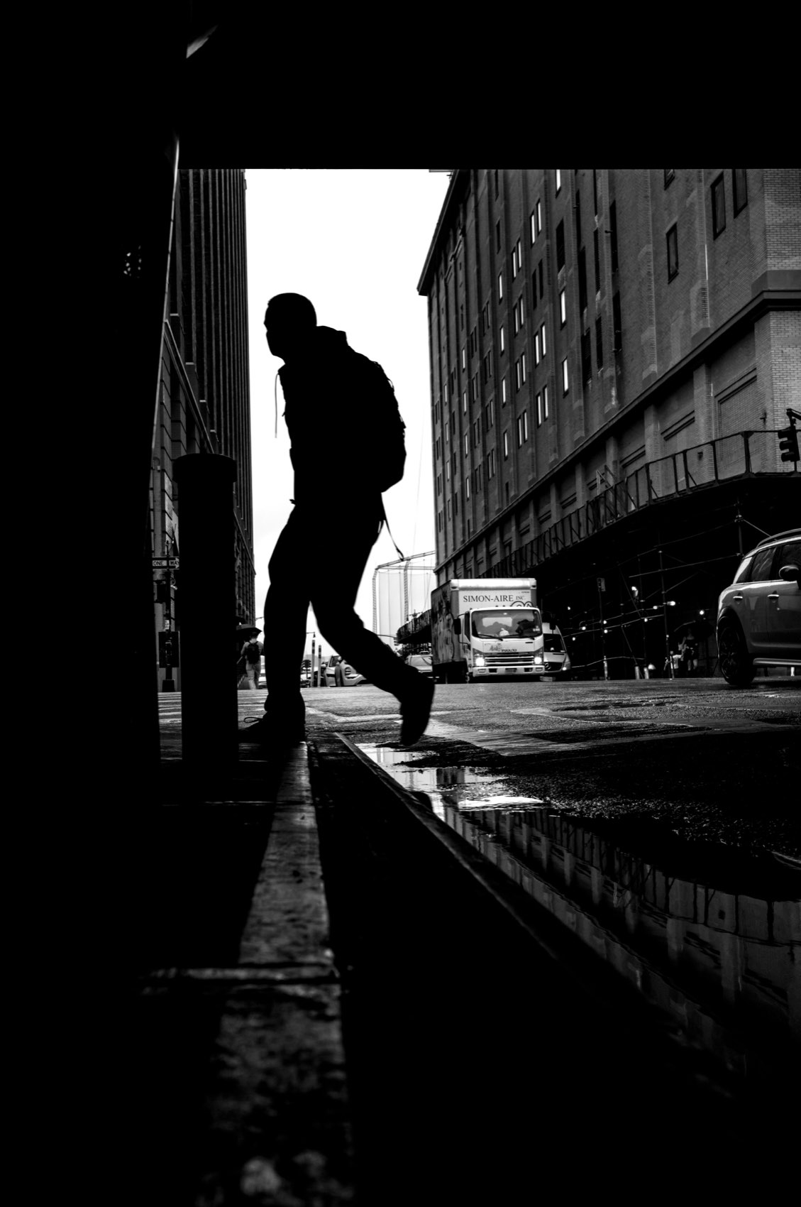 A man mid-stride, reduced to a pure black silhouette against a bright street beyond an underpass.