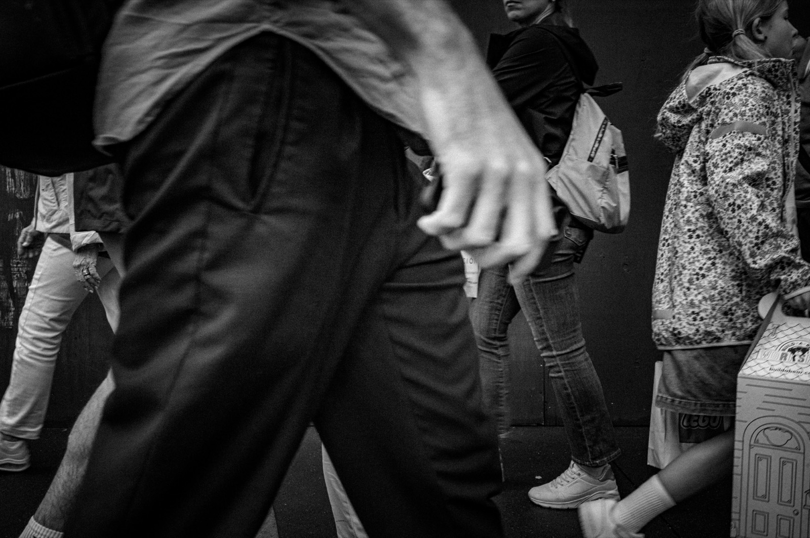 Legs and hands of pedestrians crossing frame in close-up, motion caught mid-stride.
